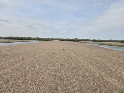 Wide view of a sandy, gravel-covered recharge area with shallow water channels on both sides and a tree line in the background at Cottonwood Ranch in Nebraska.