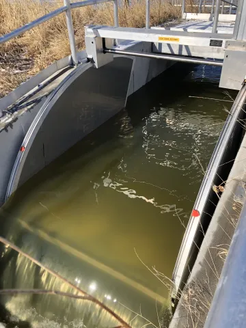 Water flowing through a metal hydraulic control structure beneath an access platform.