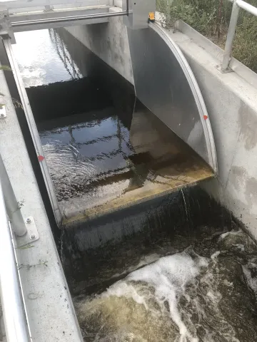 Water flowing through a gated concrete and metal flow control structure.