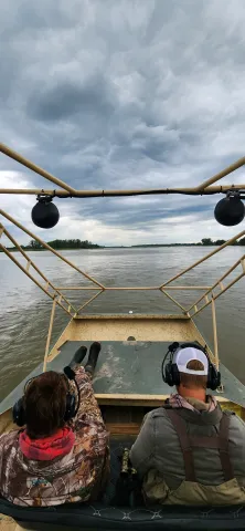 Two researchers wearing headsets ride in a survey boat on a wide river.