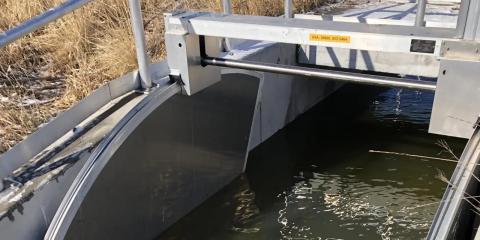 Water flowing through a metal hydraulic control structure beneath an access platform.