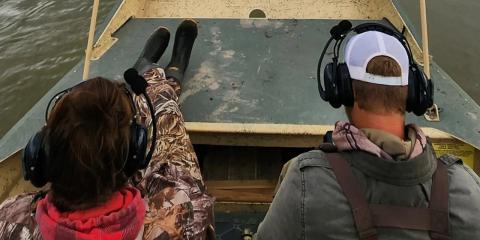 Two researchers wearing headsets ride in a survey boat on a wide river.